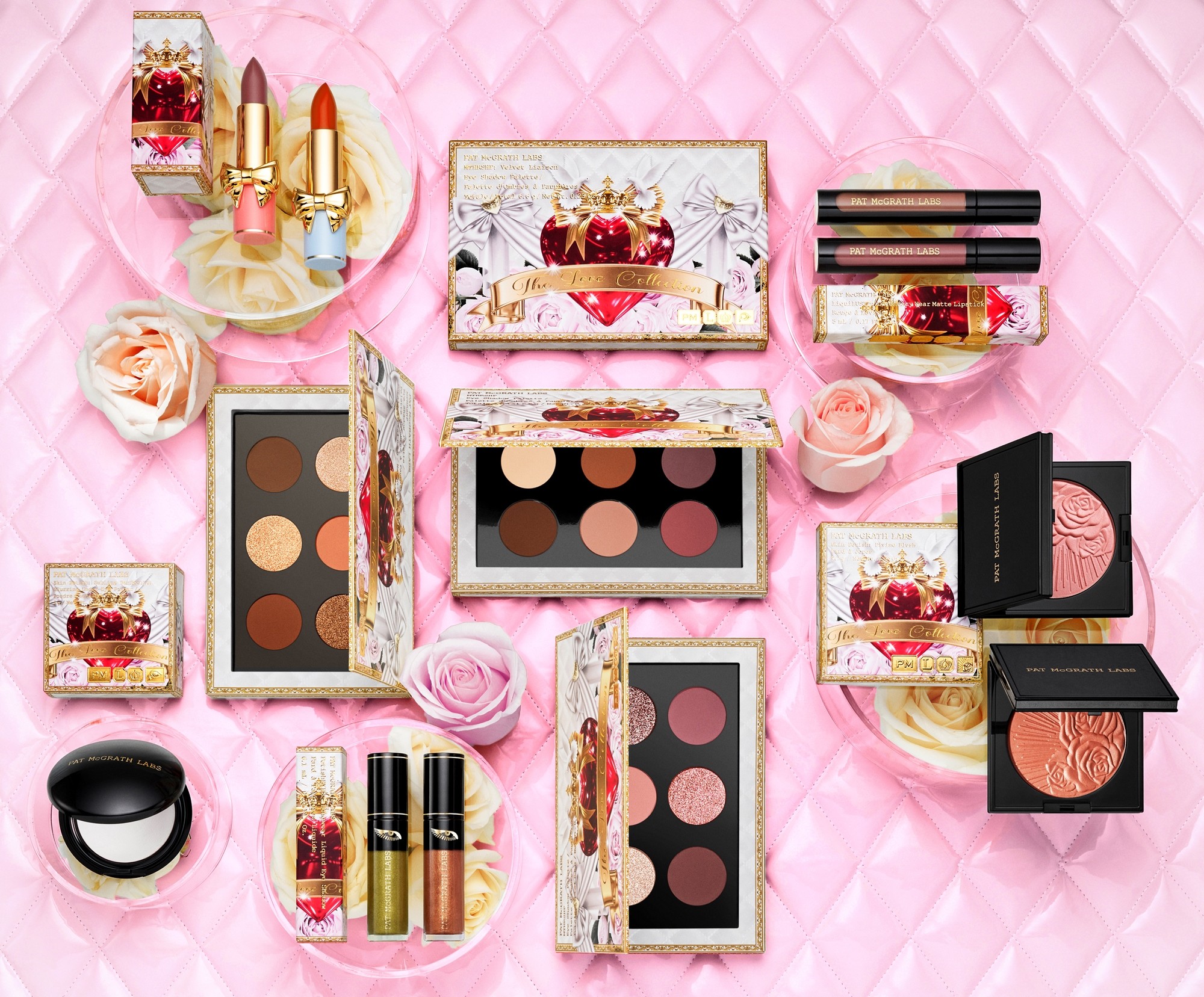 A flat-lay of Pat McGrath Labs products on quilted pink β eyeshadow palettes, lipsticks, blushes and compacts arranged with roses.