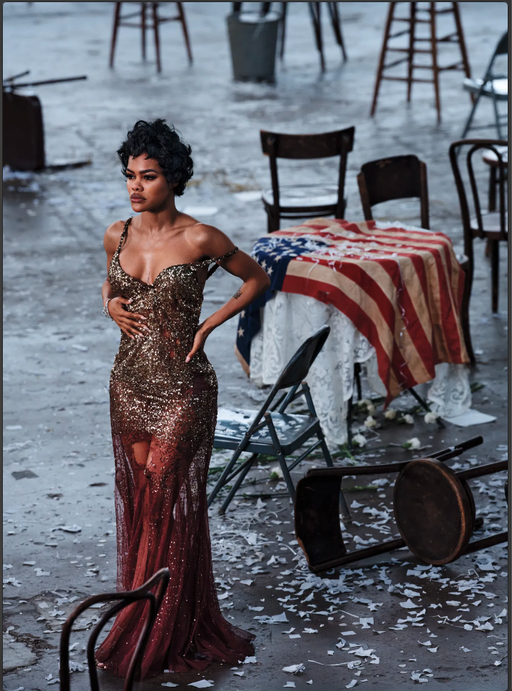 Teyana Taylor in a sequined gold-to-burgundy gown, hands on her hips, standing amid an overturned aftermath-of-the-party set.