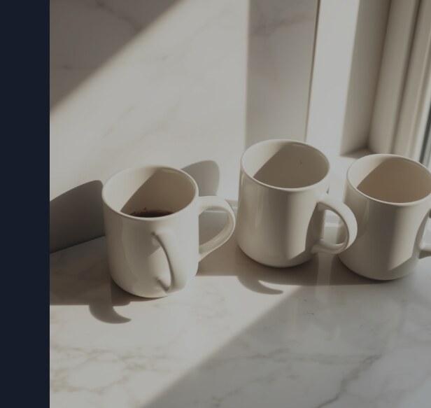 Three identical white ceramic mugs left on a marble counter, each half-finished and gone cold, the record of a morning interrupted three times.